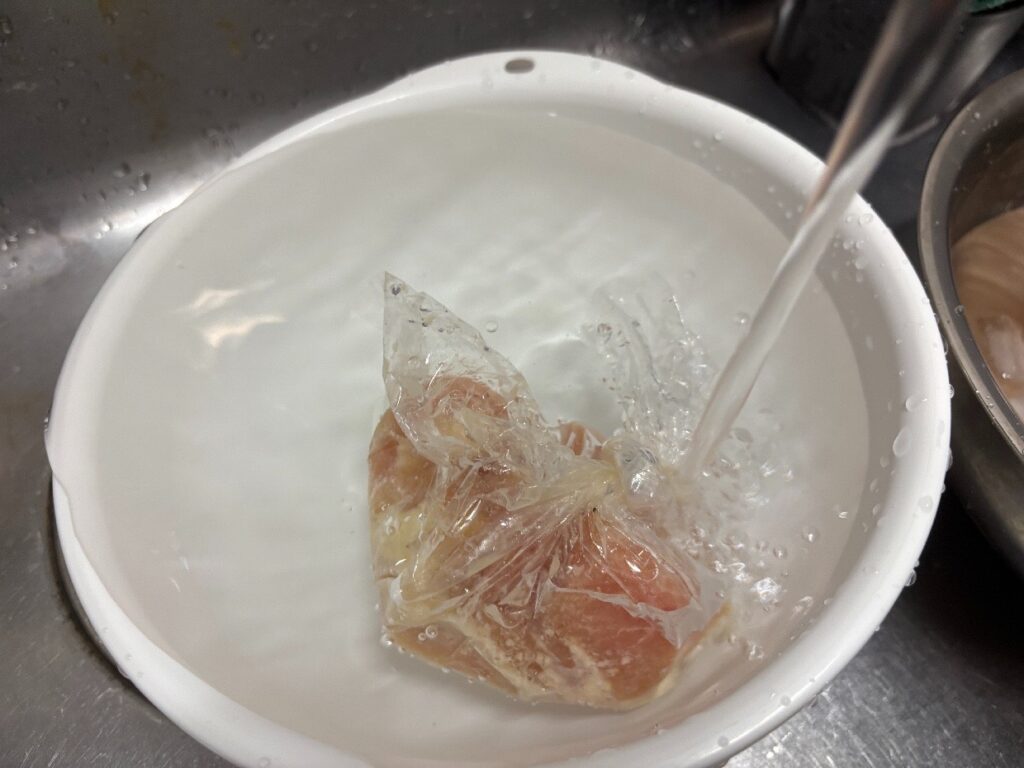 袋の口を閉じたまま流水を当てて解凍している鶏むね肉