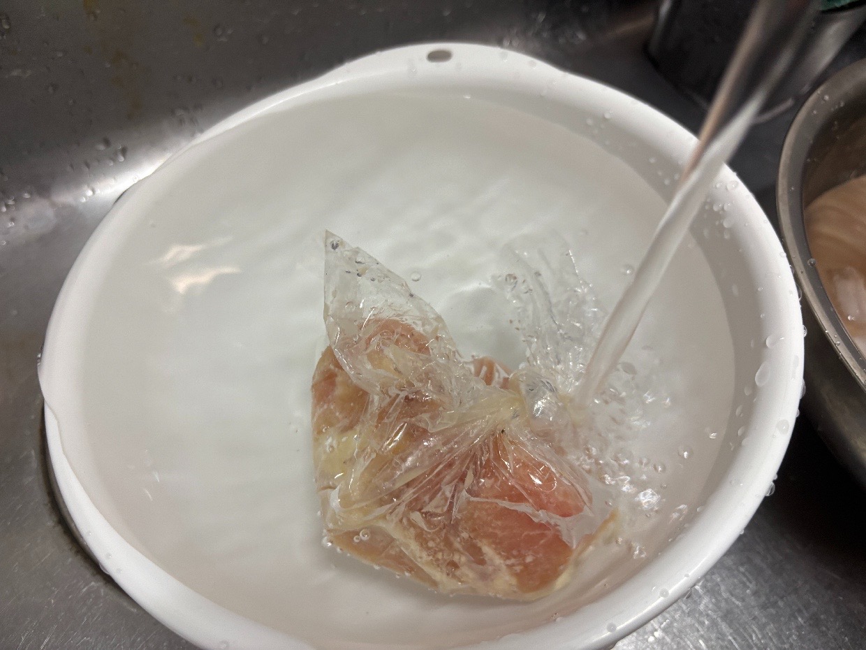 袋の口を閉じたまま流水を当てて解凍している鶏むね肉